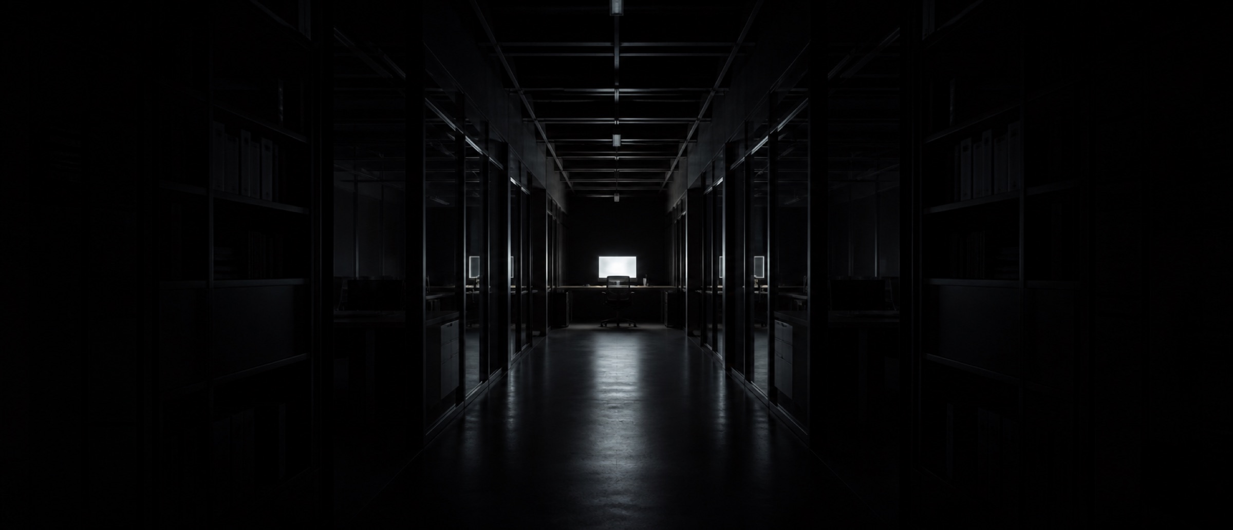 A dark office corridor at night, a single monitor glowing at the far end